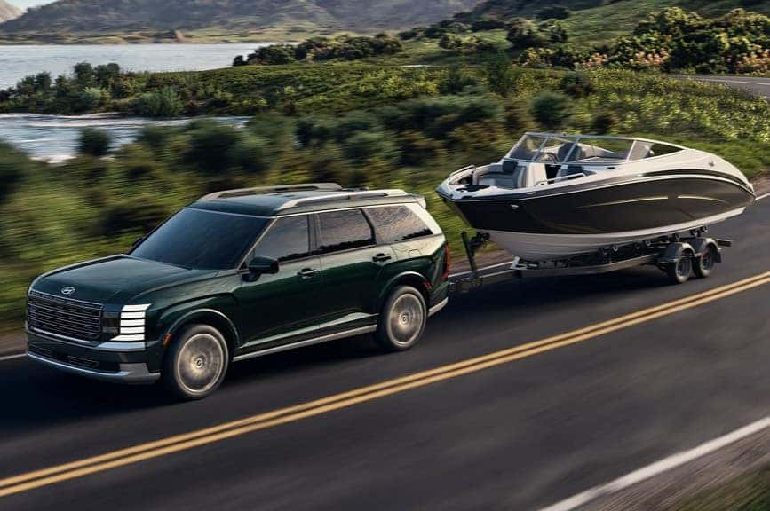 2026 Hyundai Palisade driving on a scenic road towing a boat showing its V6 performance and all-wheel drive capability