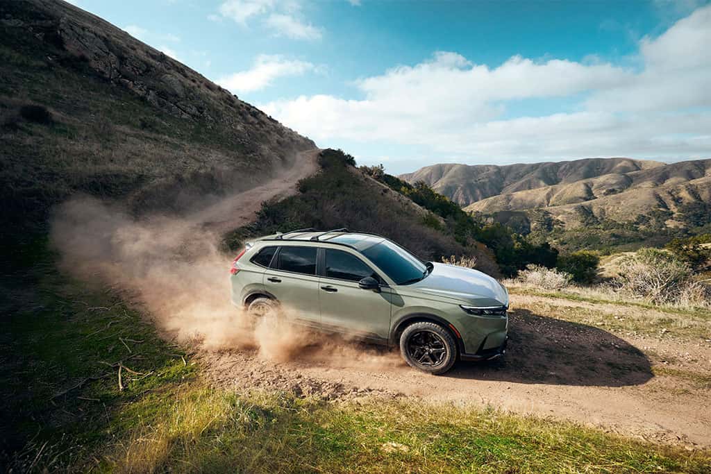 2026 Honda CR-V TrailSport Hybrid driving down a hill off-road in ash green metallic color