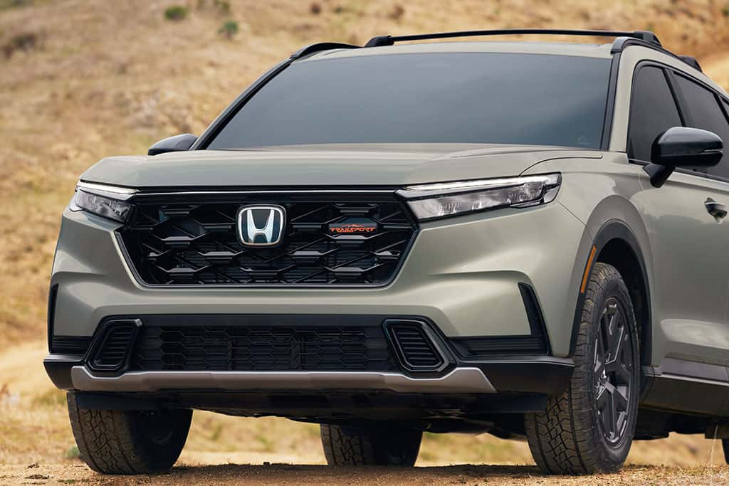2026 Honda CR-V TrailSport Hybrid showing off front grill with badging in ash green metallic color parked off-road