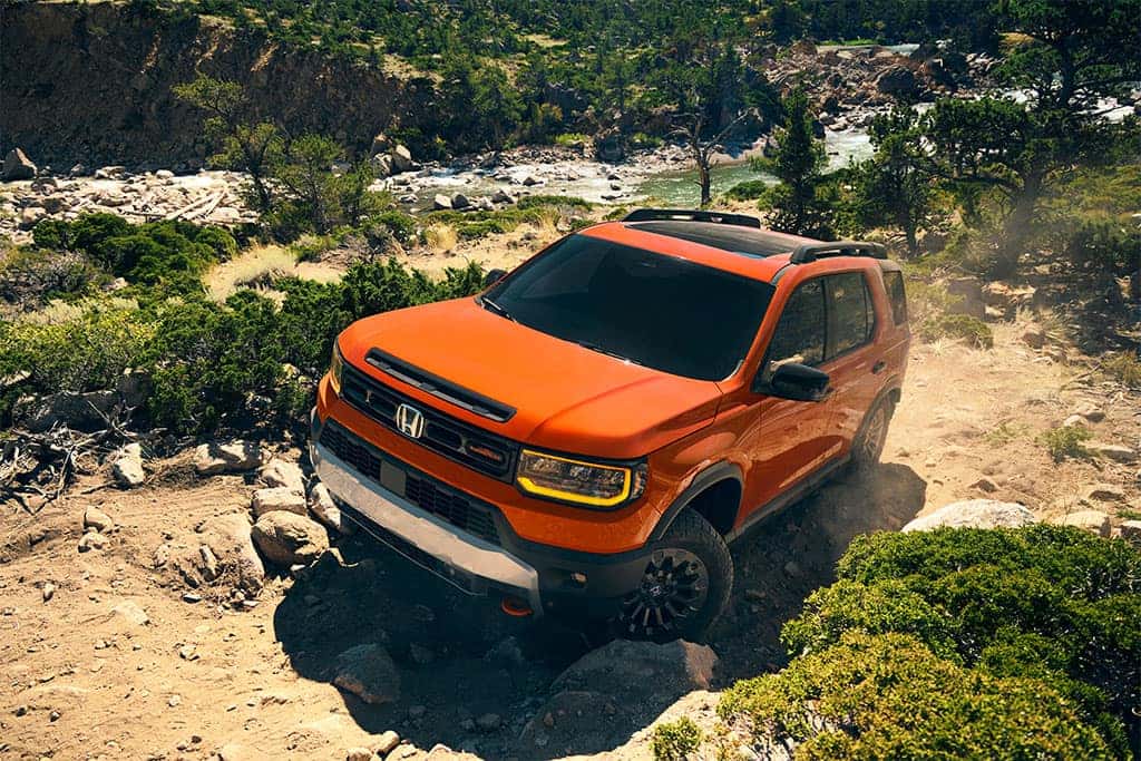 2026 Honda Passport TrailSport driving offroad near a river in sunset orange