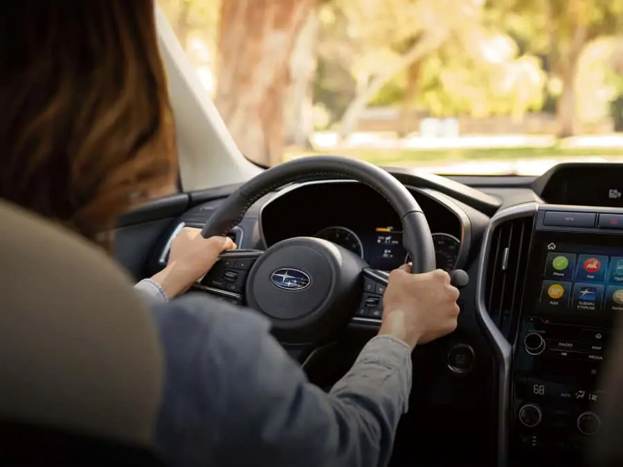 Woman driving a Subaru with both hands firmly holding the steering wheel. 