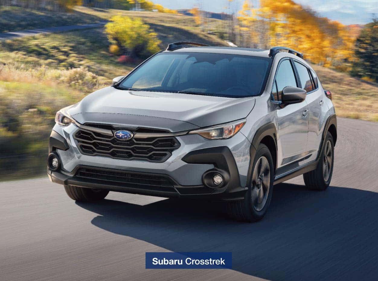 2026 Subaru Crosstrek driving on a scenic road lined with autumn trees.