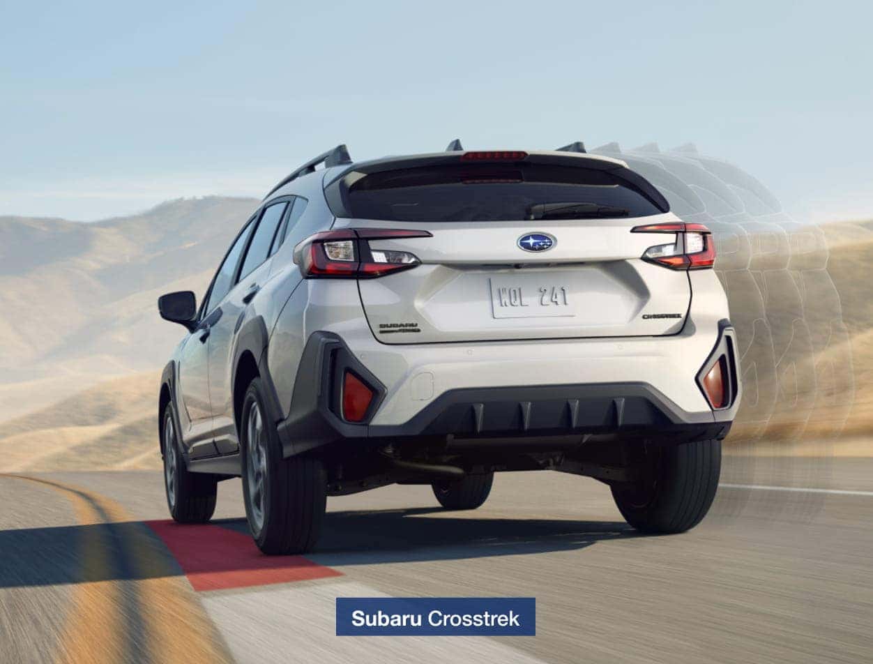 2026 Subaru Crosstrek driving on a scenic road with hills in the background.
