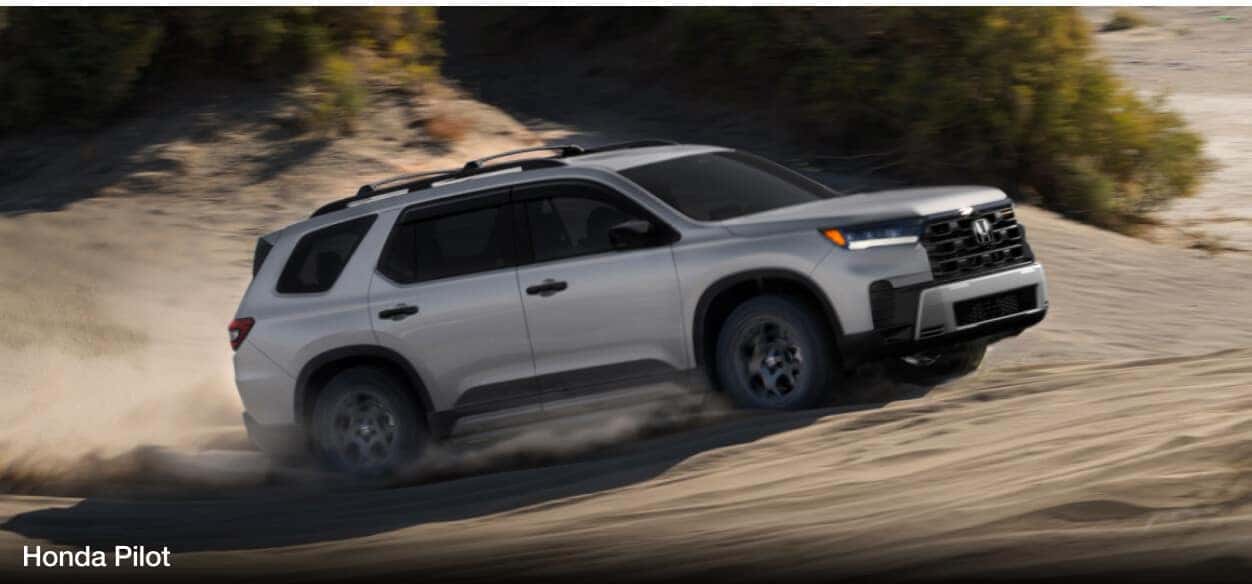 A gray Honda Pilot offroads on a sandy hill.