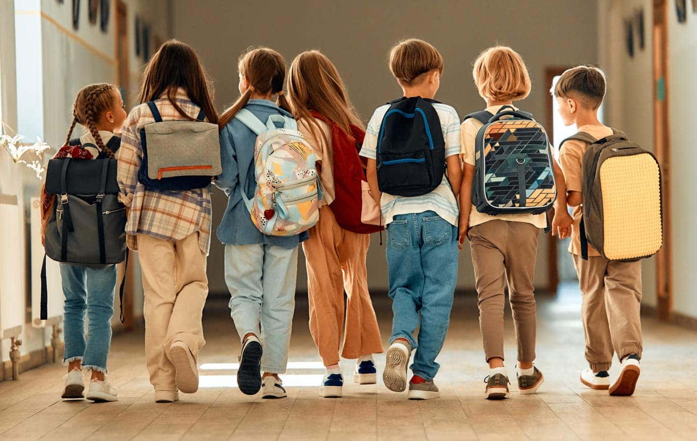 Group of students wearing backpacks walking together through a school hallway.