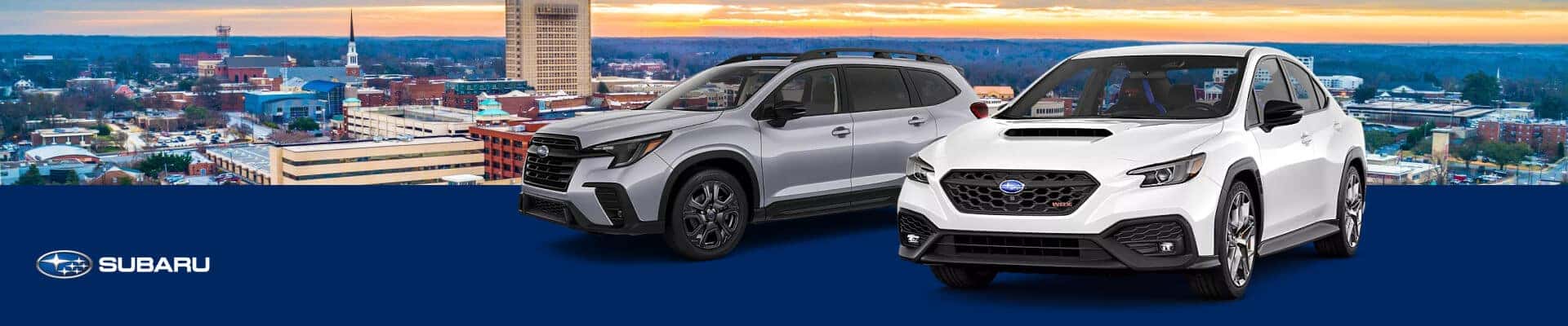 A silver 2027 Subaru Ascent and a white 2027 WRX isolated over an aerial view of the Greenville NC skyline.