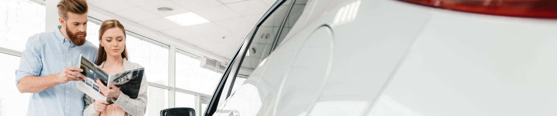 Couple reviewing vehicle information beside a white SUV inside a dealership showroom.