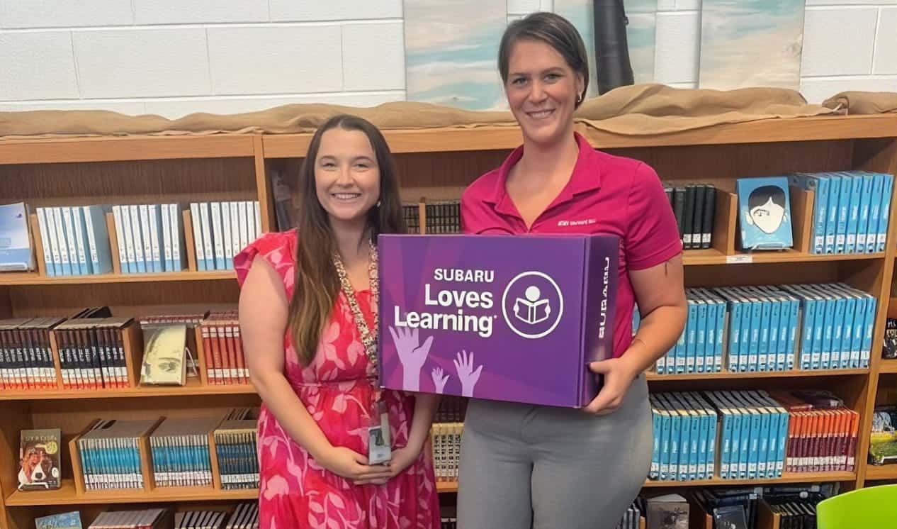 Two women holding an education donation box in front of bookshelves.