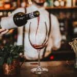 Close up shot of a bartender pouring red wine into a glass. Hospitality, beverage and wine concept.