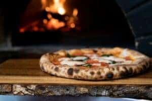 A delicious pizza coming out of a wood burning oven ready to be cut