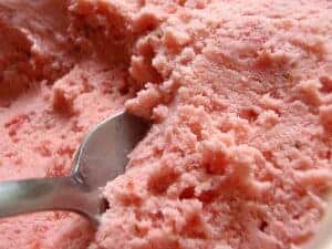 A cold metal spoon scooping into a big bowl of strawberry ice cream