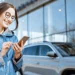 Woman in front of car on her phone smiling