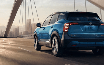 Rear view of a blue Kicks crossing a bridge with a city skyline in the distance
