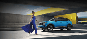 2026 Nissan Kicks parked at a modern concrete building with a model in a blue dress in the foreground