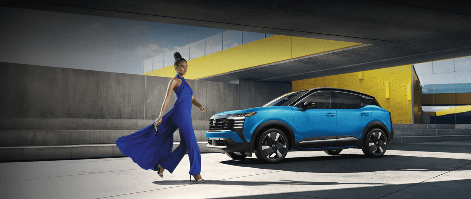 2026 Nissan Kicks parked at a modern concrete building with a model in a blue dress in the foreground