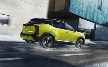Rear three-quarter view of a yellow Kicks driving on a wet street