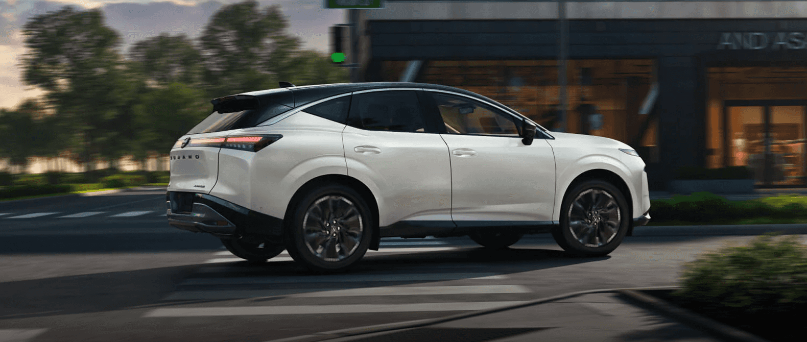 2026 Nissan Murano driving past a modern storefront at dusk