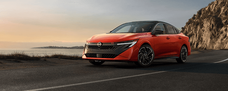 Front three-quarter view of an orange Sentra SR on a coastal road at sunset