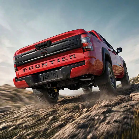 2026 Nissan Frontier PRO-4X kicking up dirt on a trail, rear three-quarter view showing the tailgate and 4WD stance