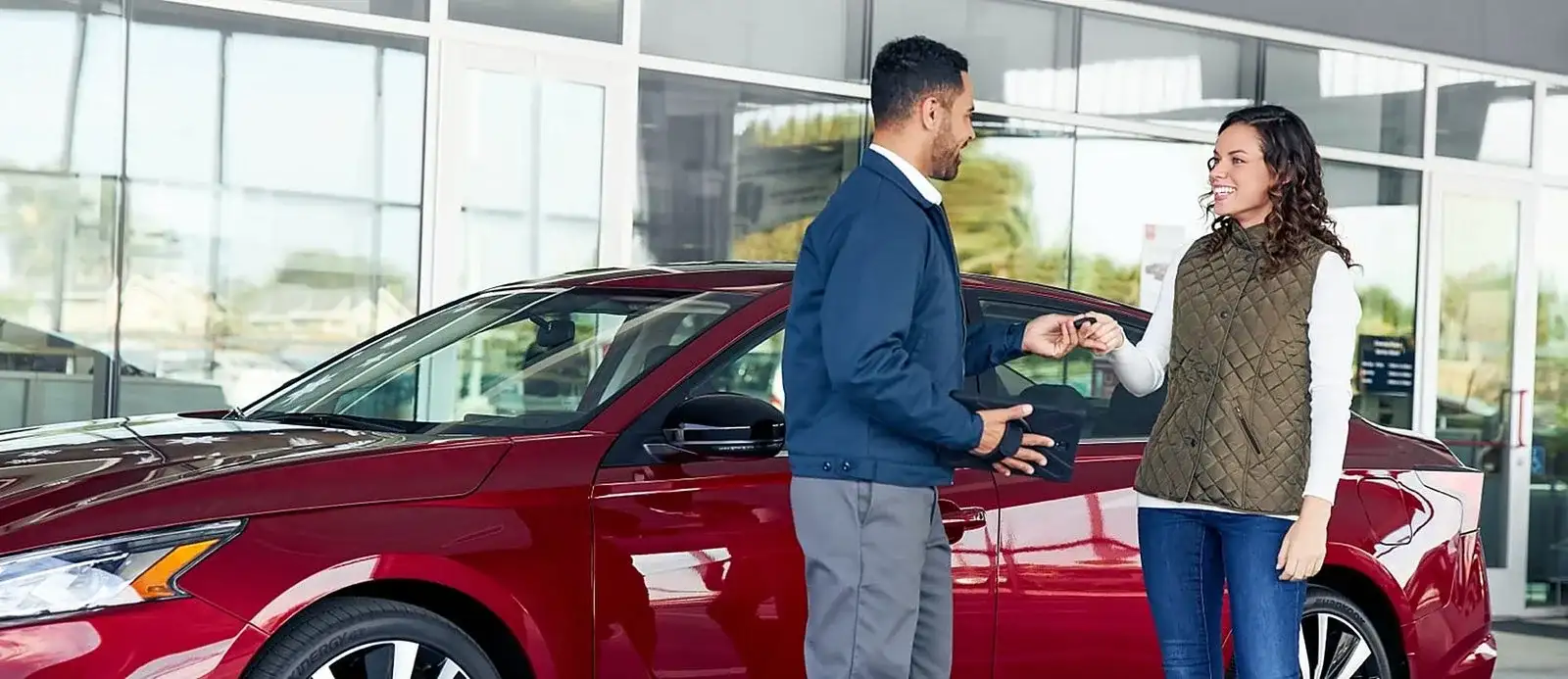 A customer handing over the keys to their trade-in at I-90 Nissan in Sheffield Village, Ohio, in front of a Nissan sedan