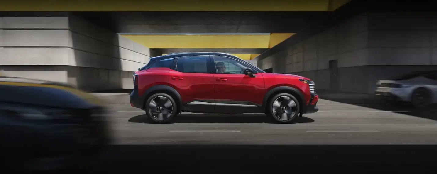 Nissan Kicks in red, side profile, driving through an urban underpass