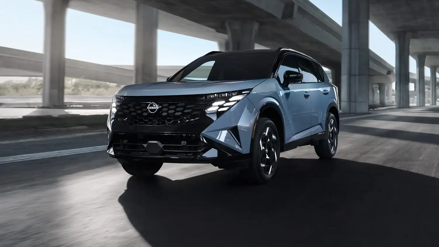 A 2027 Nissan Rogue Hybrid driving on a road beneath a concrete overpass