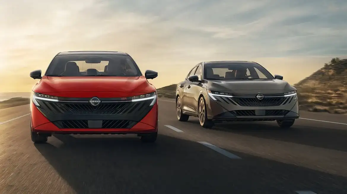 Two 2027 Nissan Sentras, one red and one grey, driving side by side on a coastal road at sunset