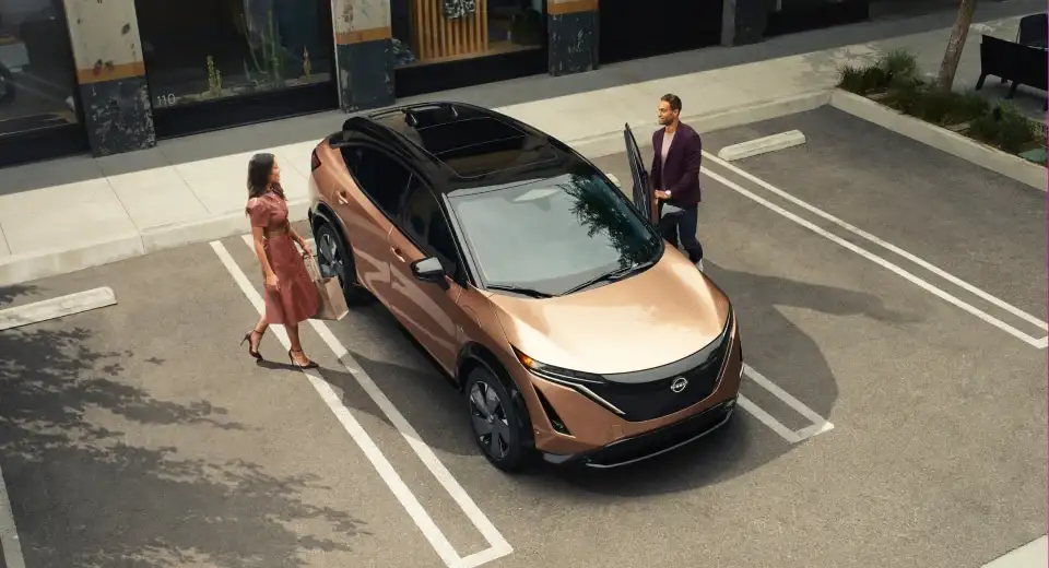A copper Nissan Ariya parked in a city street bay, two people walking back to it