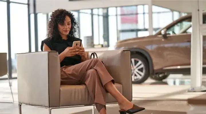 A customer waiting in the showroom lounge at I-90 Nissan, with a vehicle on display behind her