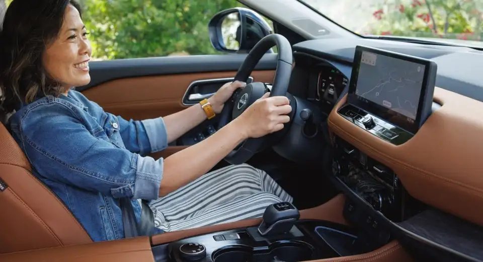 A driver at the wheel of a Nissan with a tan leather interior, navigation showing on the centre screen