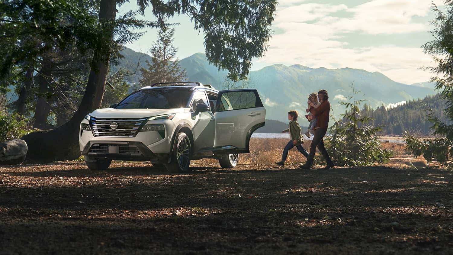 A white Nissan Rogue parked at a mountain trailhead with a rear door open and a family walking toward it