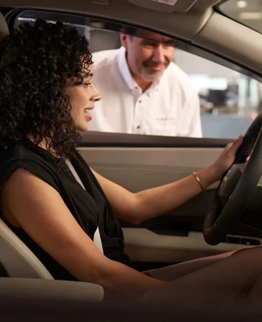 A Nissan salesperson leaning at the open window to talk to a customer sitting in the driver's seat
