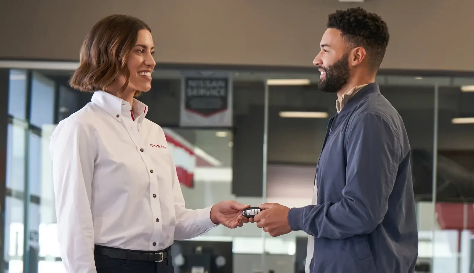 A Nissan service advisor handing a key back to a customer under the Nissan Service sign in the service reception
