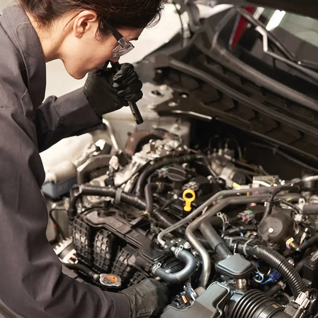 A Nissan technician with a flashlight inspecting an engine bay under an open hood