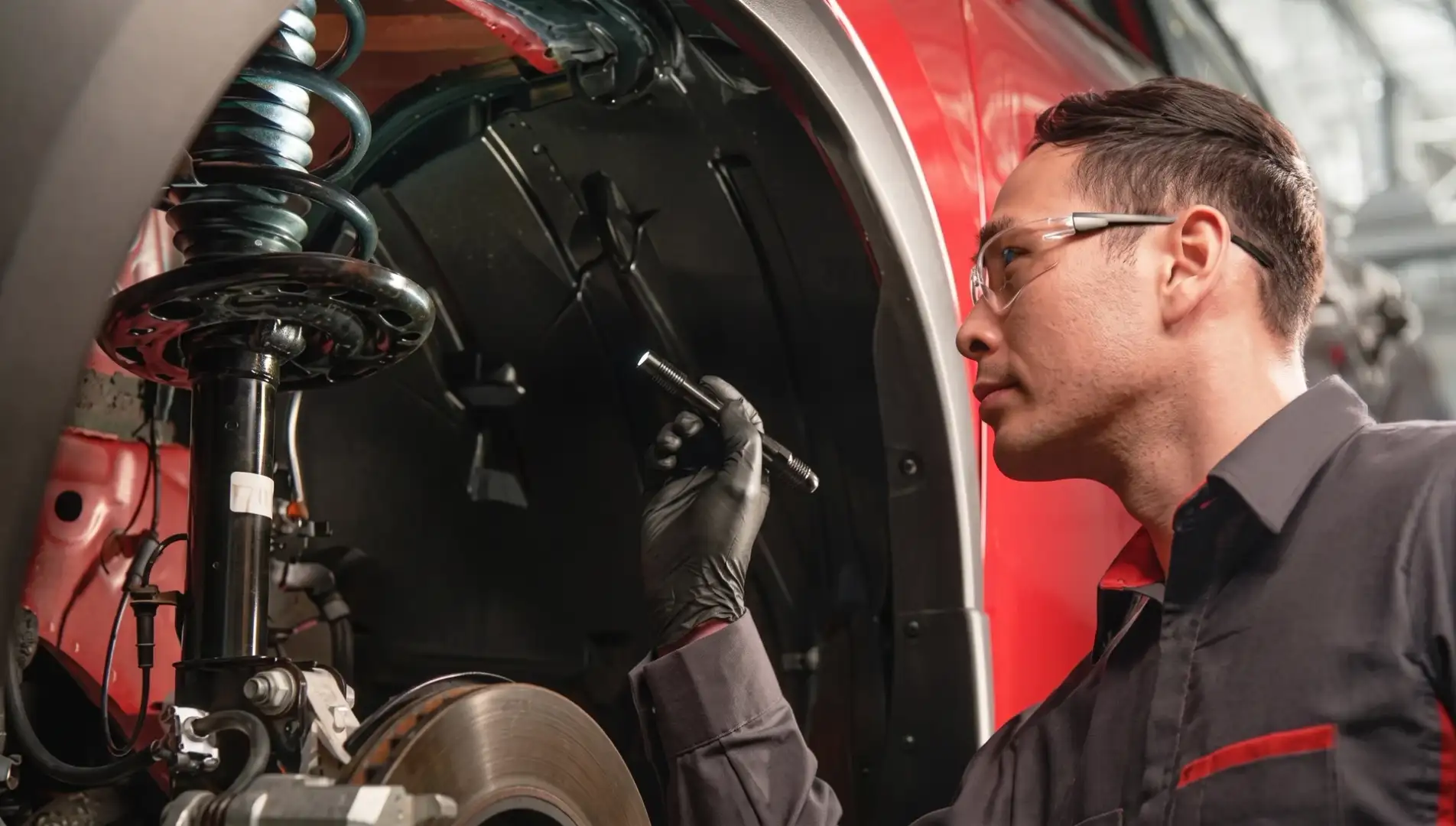 A Nissan technician in safety glasses inspecting the suspension inside a wheel arch