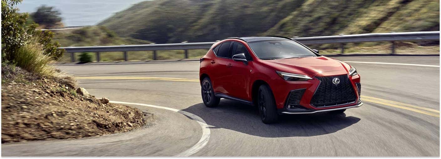 Front three-quarter view of a red 2026 Lexus NX SUV driving on a winding coastal road.