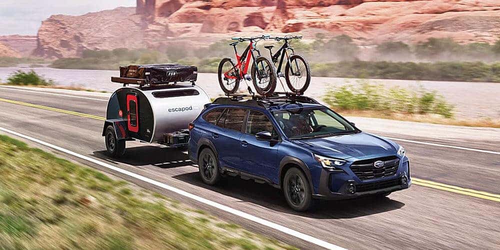 2025 Subaru Outback Driving Towing Camper on Highway