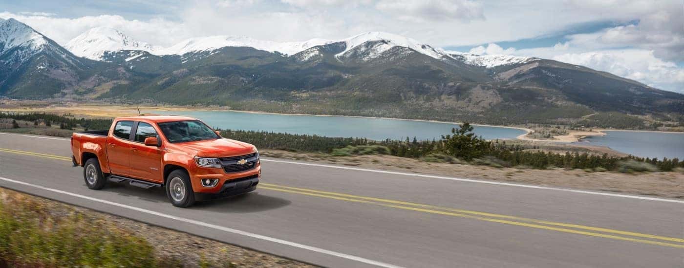 An orange 2016 Chevy Colorado Z71 is shown driving past mountains.