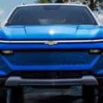 A blue 2025 Chevy Equinox EV for sale is shown parked near water.