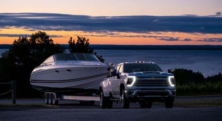 A white 2025 Chevy Silverado 3500 HD is shown from the front at an angle while towing a boat.