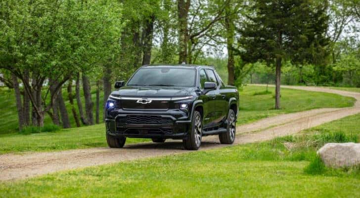 A black 2024 Chevy Silverado EV for sale is shown driving on a trail.