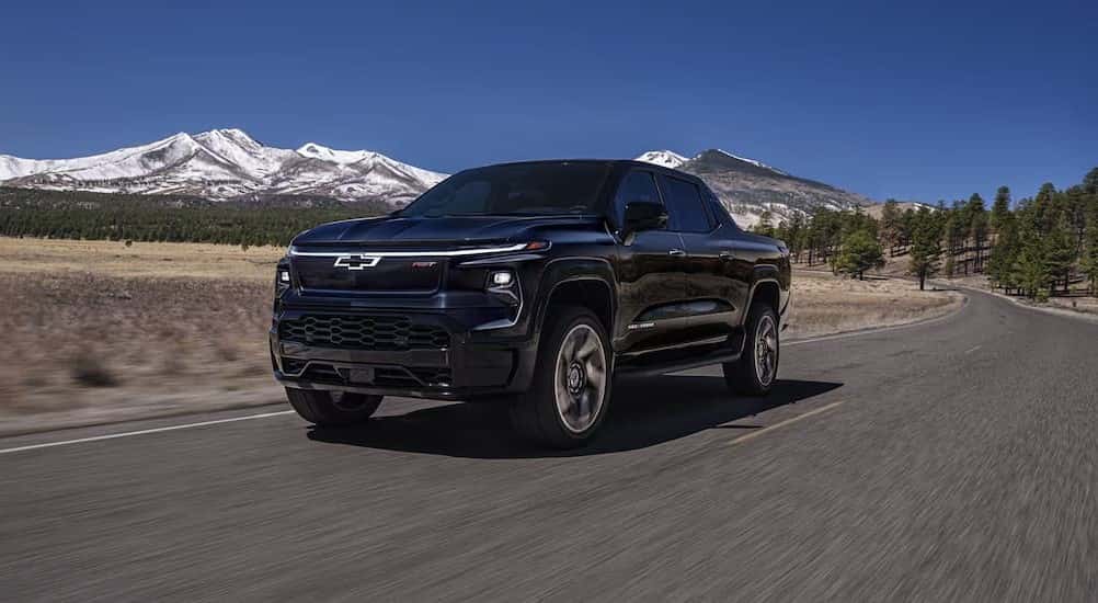 A blue 2025 Chevy Silverado RST is shown driving on a highway near a mountain.