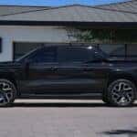 A black 2025 Chevy Silverado EV RST is shown parked near a white house.
