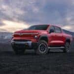 A red 2025 Chevy Silverado EV Trail Boss is shown parked under a beautiful sky.