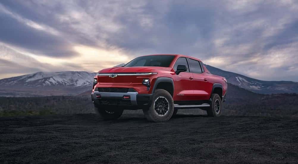 A red 2025 Chevy Silverado EV Trail Boss is shown parked under a beautiful sky.