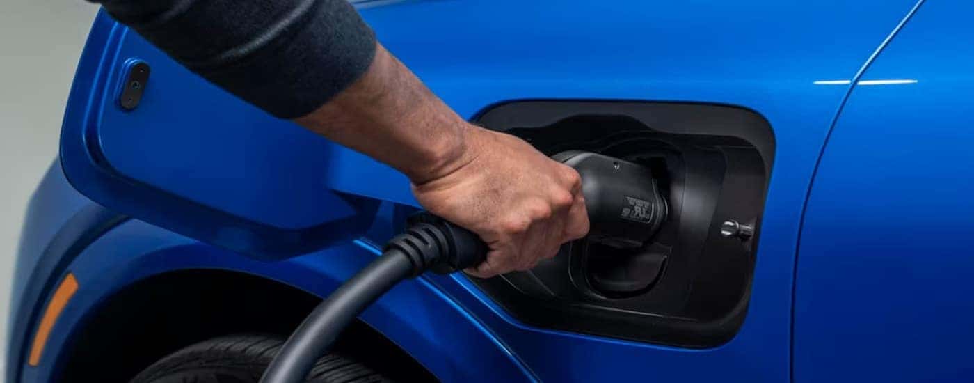 A person is shown charging a blue 2025 Chevy Equinox EV for sale near University City.
