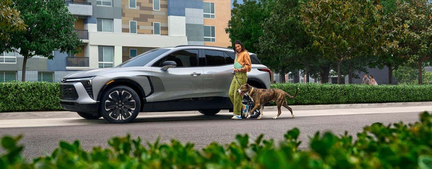 A woman walking by a white 2025 Chevy Blazer EV for sale near University City parked by a curb.