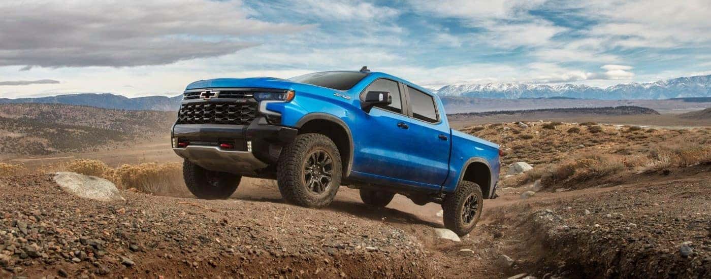 A blue 2024 Chevy Silverado 1500 ZR2 driving up a dirt hill.