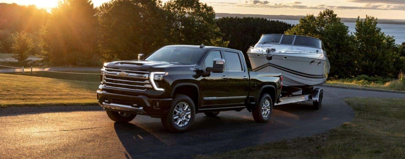 A black 2024 Chevy Silverado 2500 HD High Country for sale near University City towing a boat.