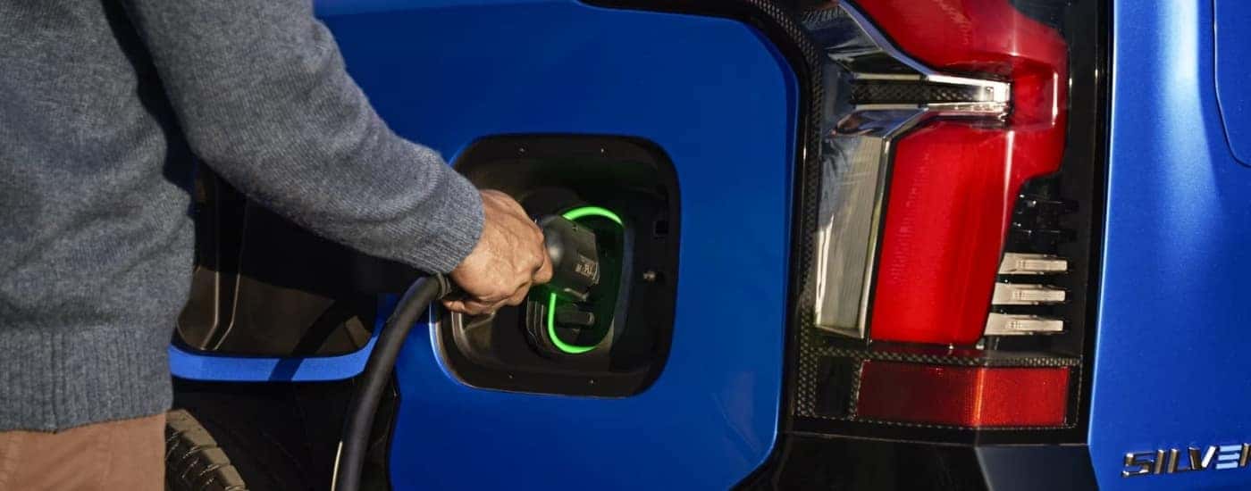 A person charging a blue 2024 Chevy Silverado EV.